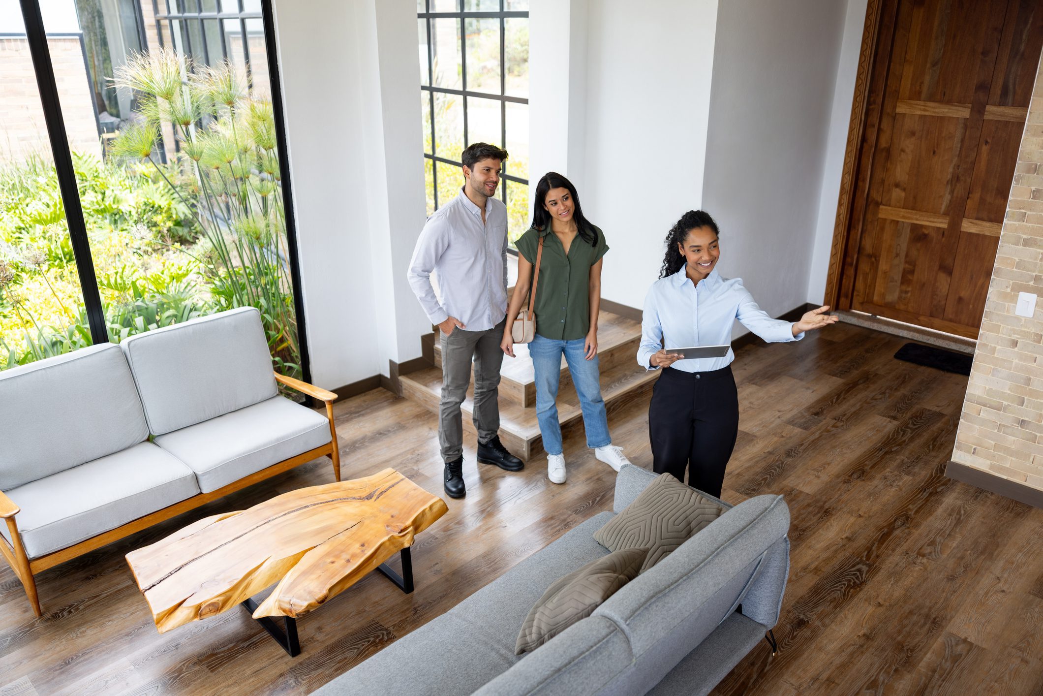 Happy real estate agent showing a house for sale to a Latin American couple - home ownership concepts